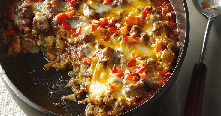 a skillet filled with meat and cheese on top of a table next to a fork