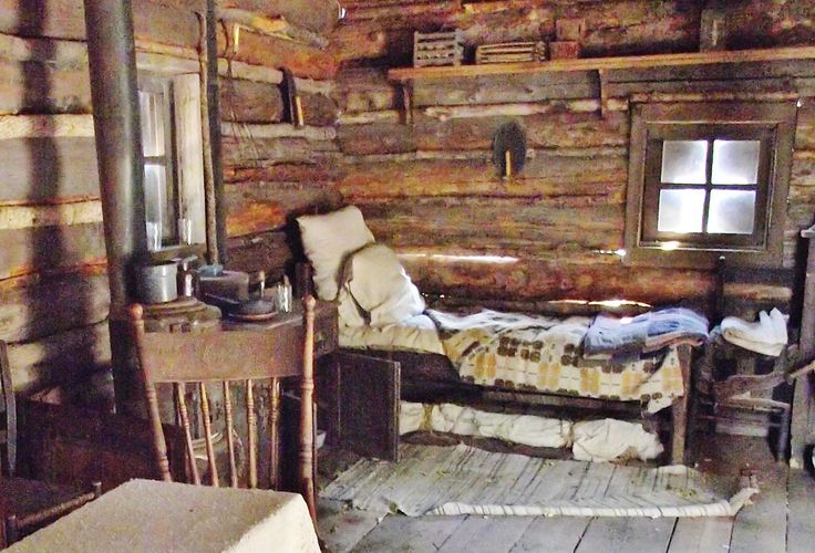 an old log cabin with a small bed and chair in it's center room