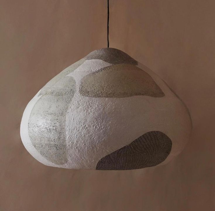 a white and gray object hanging from a string on a wall next to a lamp