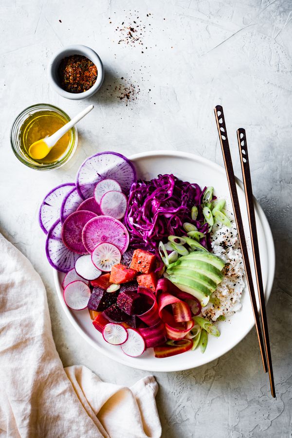 a white bowl filled with sliced vegetables next to two chopsticks and an orange