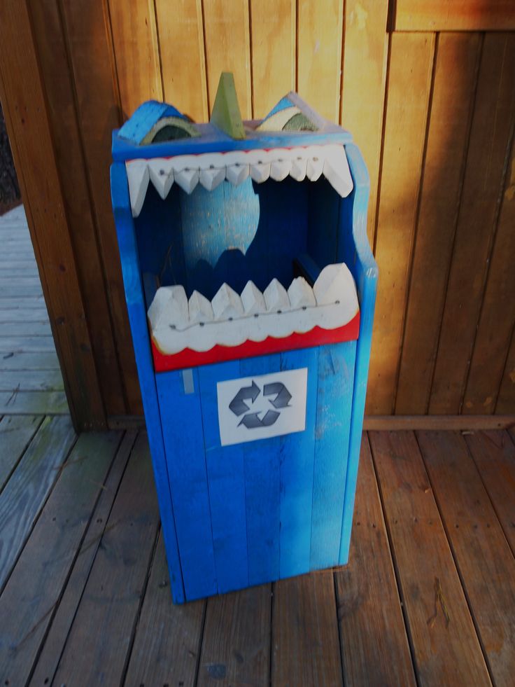 a blue box with teeth on it sitting on a wooden floor next to a fence