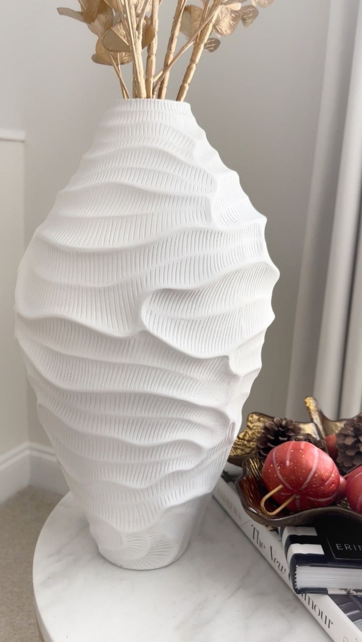 a white vase sitting on top of a table next to a book and some plants