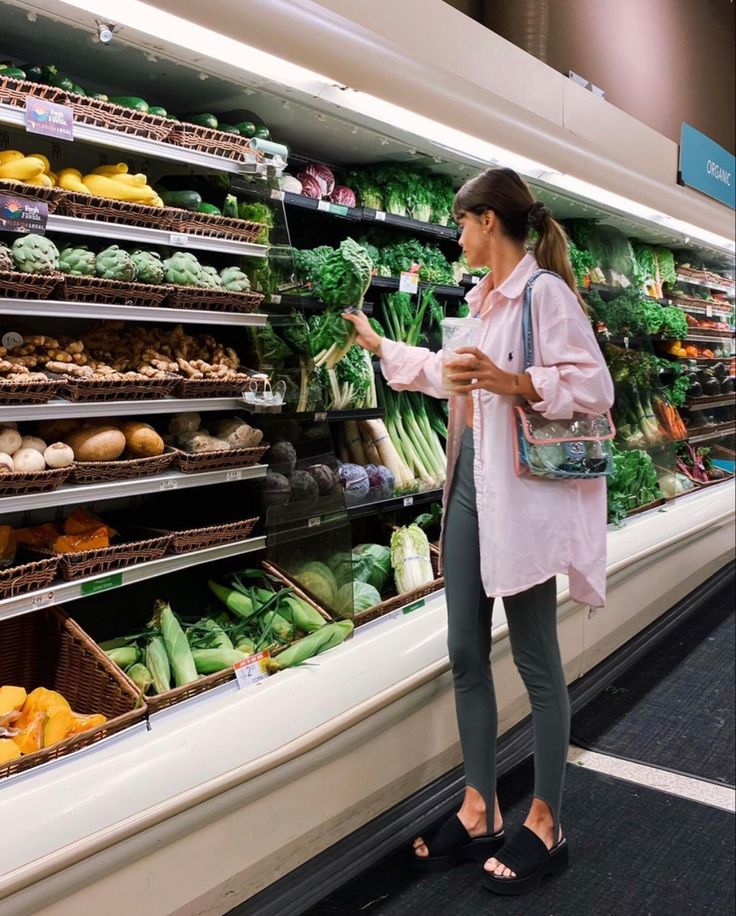 a woman standing in front of a grocery store display filled with fresh vegetables and fruits