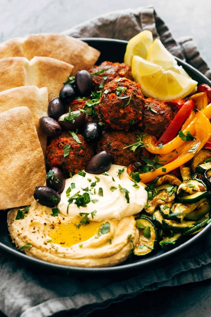 a bowl filled with meat, vegetables and pita bread on top of a table