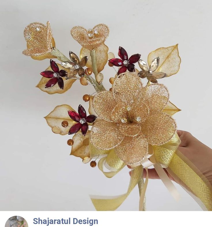 a hand holding a gold flower with red and white flowers