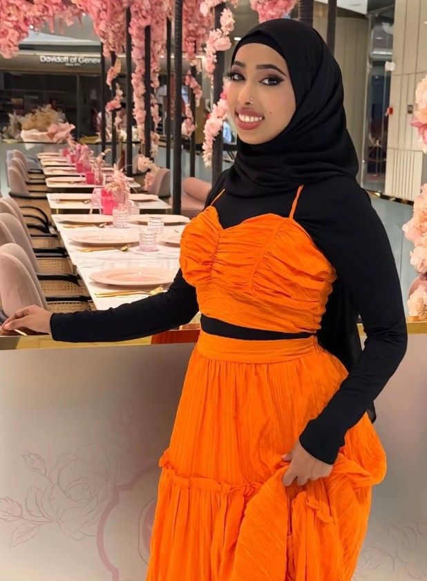 a woman in an orange dress standing next to a table with pink flowers on it