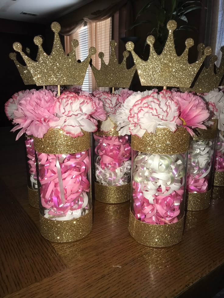 pink and white flowers in gold crown vases on a wooden table with other decorations