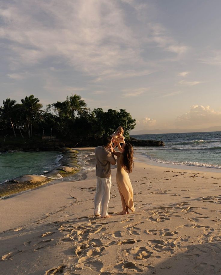 a man and woman standing on top of a sandy beach next to the ocean with palm trees in the background