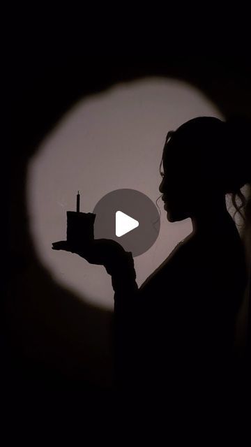 the silhouette of a woman holding a cupcake in front of a dark background with a circular light