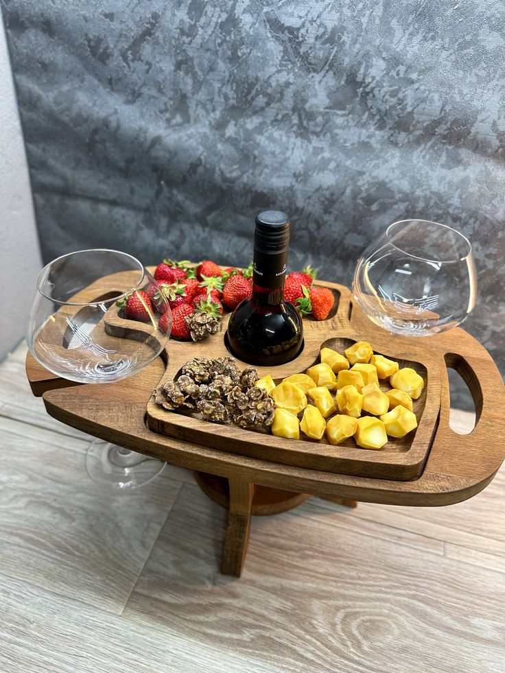 a wooden tray filled with different types of food and wine glasses on top of it