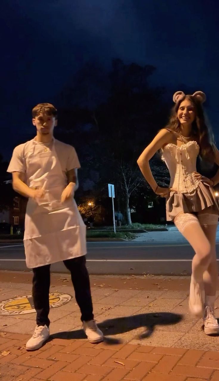 two people dressed in costumes standing on the side walk at night with their arms around each other