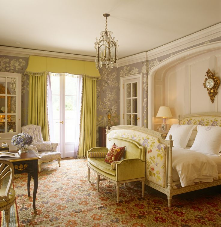 a bedroom with a bed, chair and chandelier next to a desk in front of a window