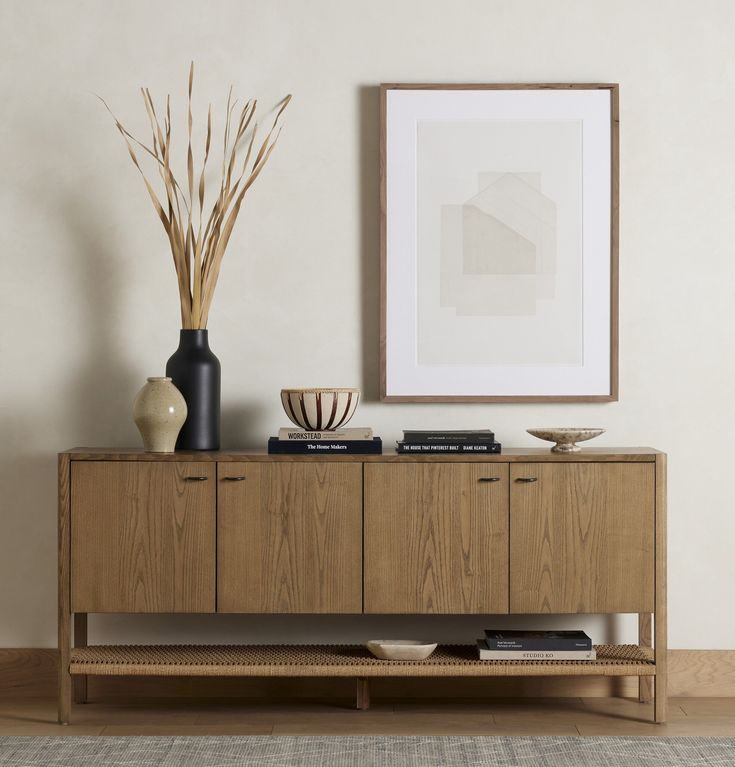 a wooden sideboard with two vases on top and a framed photograph above it