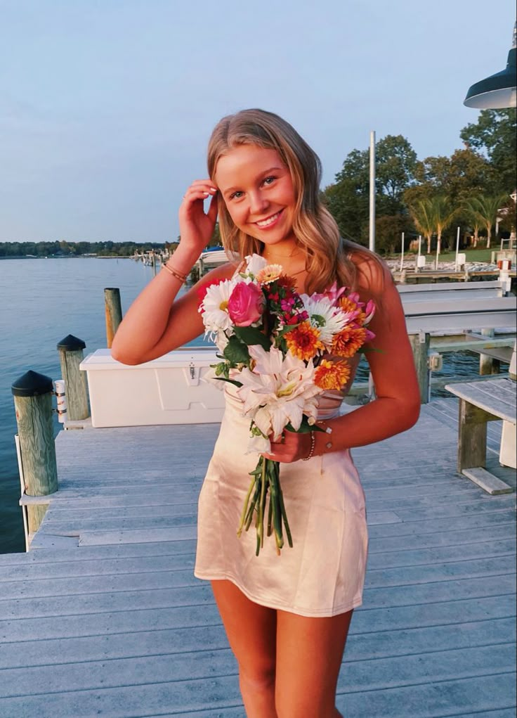 a woman is standing on a dock with flowers in her hand and talking on the phone