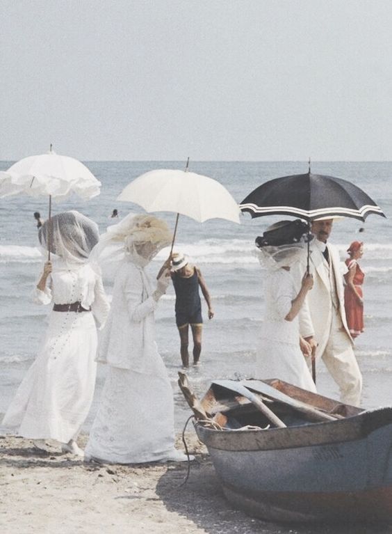 people walking on the beach with umbrellas over their heads and one person holding an umbrella