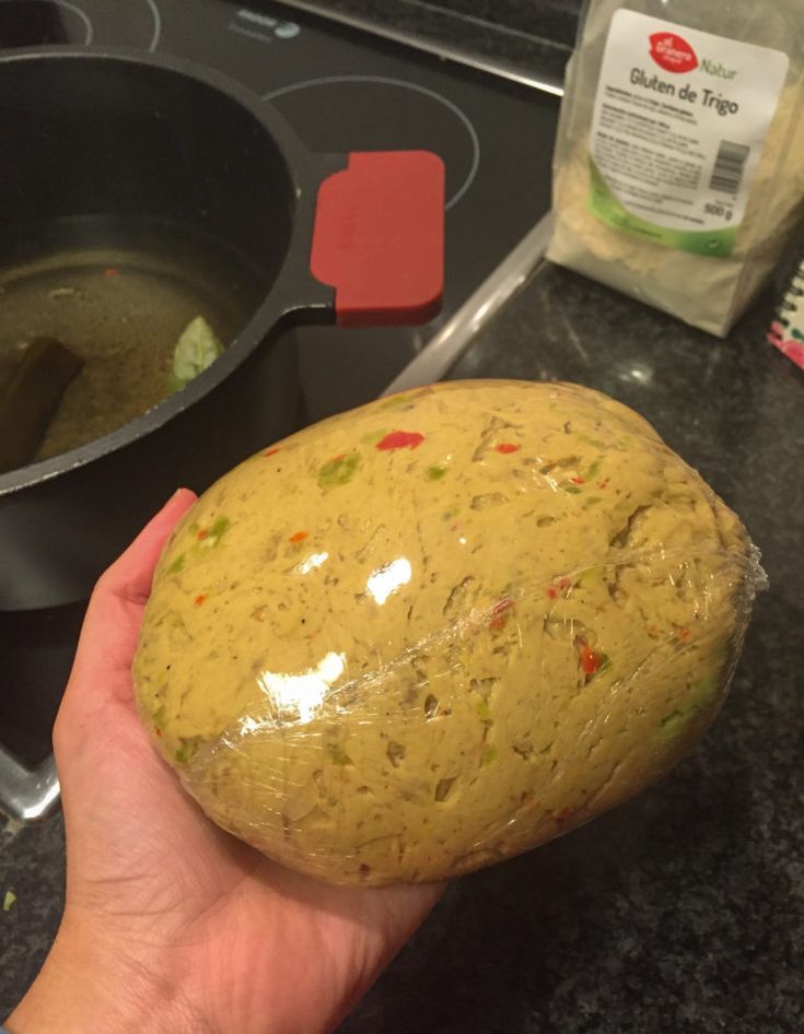 a person holding up a piece of bread in front of a stove top with some food on it