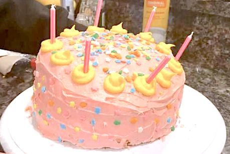 a pink birthday cake with lit candles on it