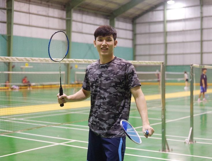 a young man holding a tennis racquet on top of a tennis court with people in the background