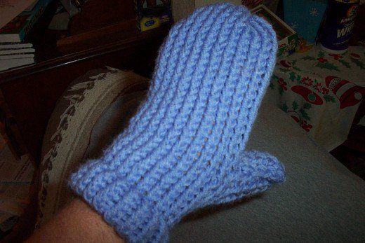 a blue knitted mitten sitting on top of a couch next to a person's hand