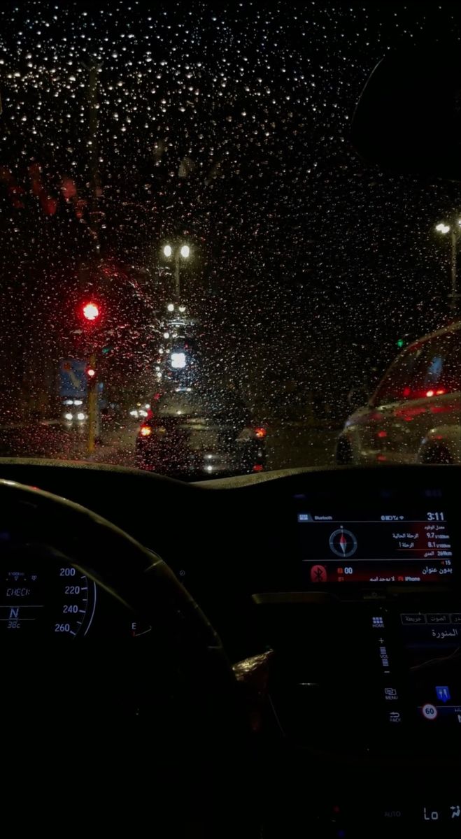 rain is falling on the windshield of a car at night with street lights in the background