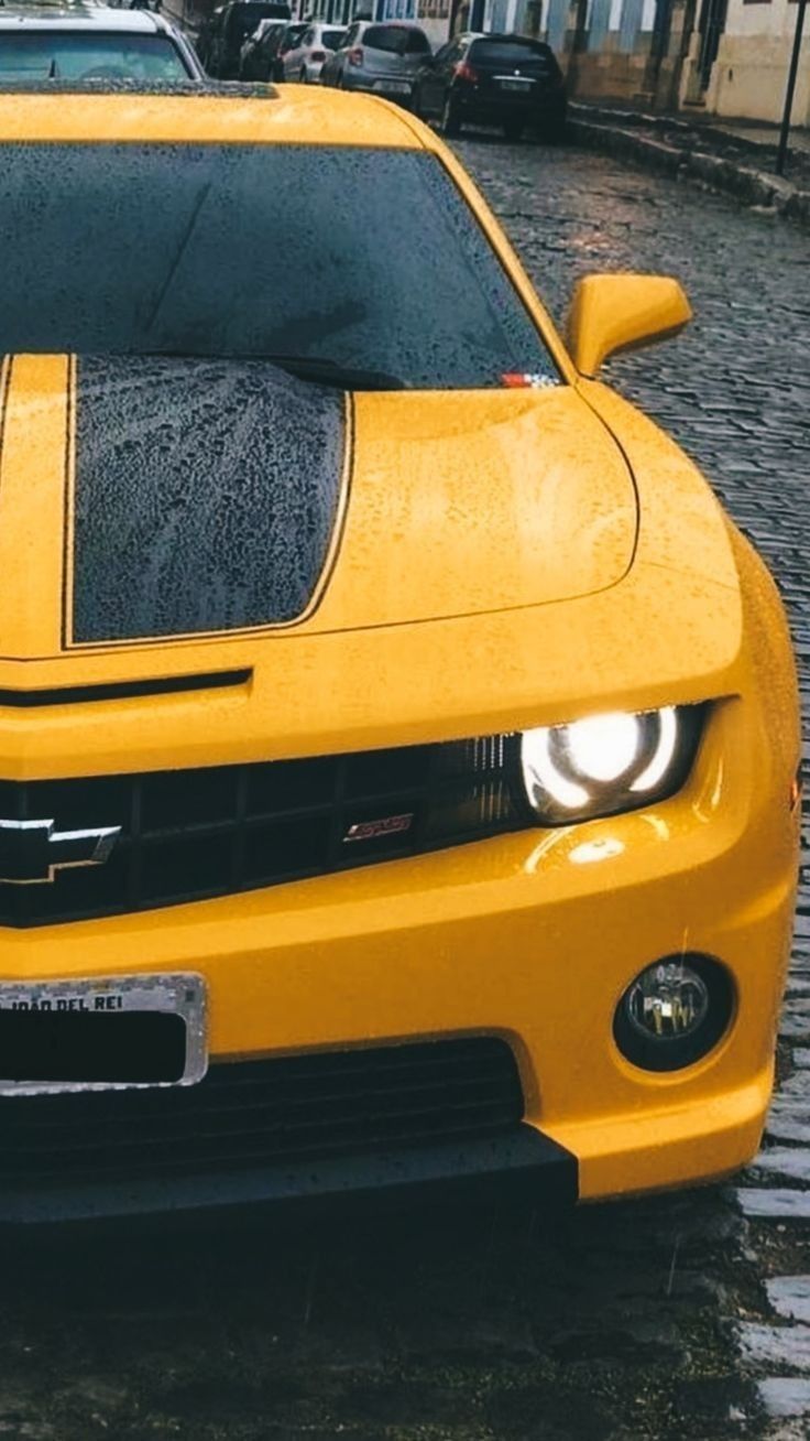 a yellow chevrolet camaro is parked in the rain