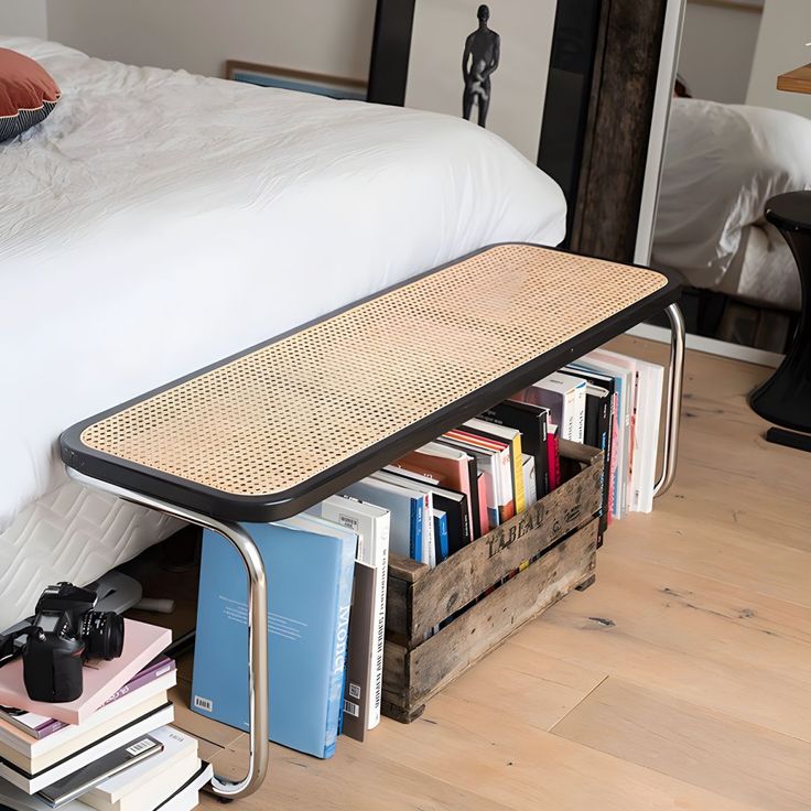 a bed sitting next to a stack of books on top of a wooden floor