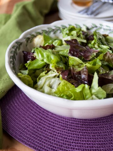 a white bowl filled with lettuce on top of a purple table cloth next to silverware