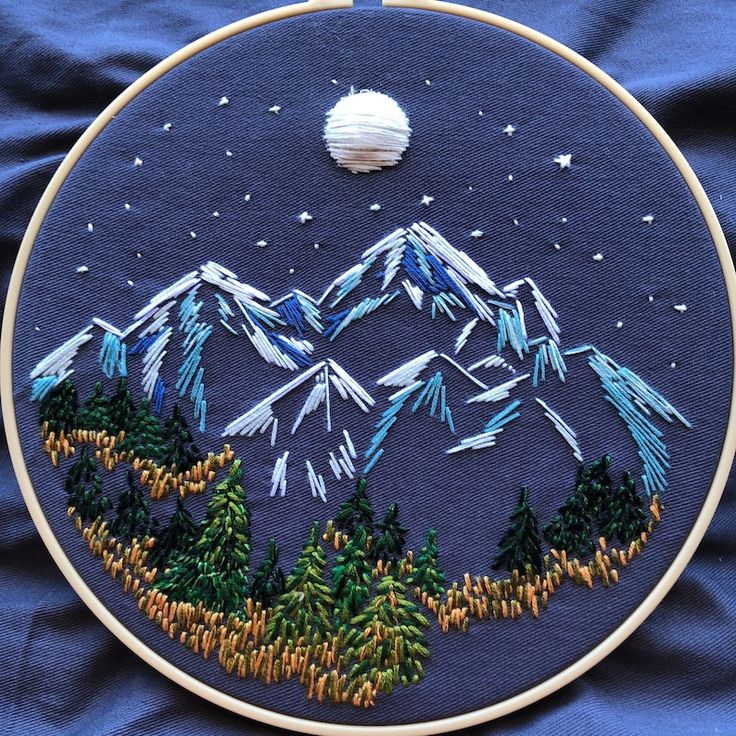 an embroidery project with mountains and pine trees on it, in the middle of blue fabric