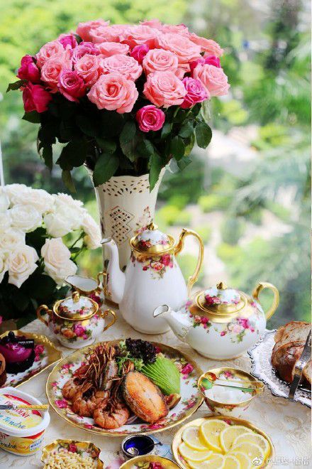 a table topped with plates and cups filled with different types of food next to a vase full of pink roses