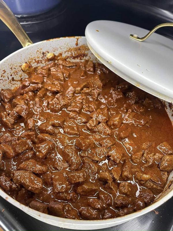 a large pot filled with meat and sauce on top of a stove next to a spatula