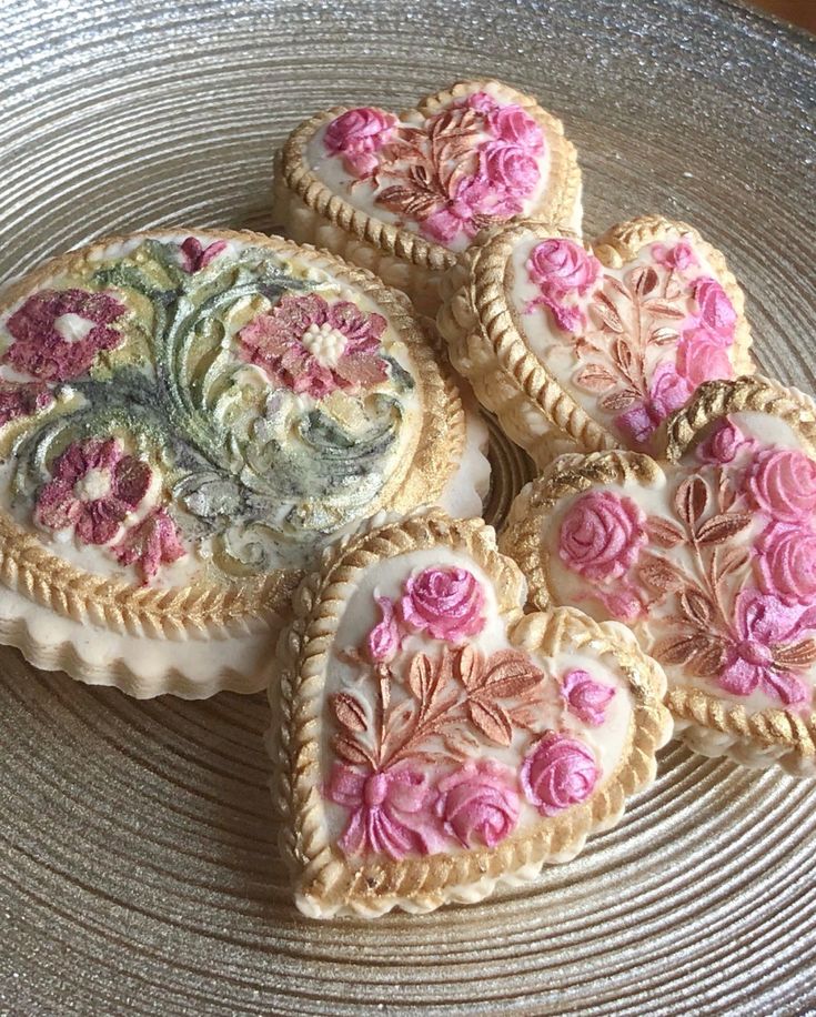 four heart shaped cookies decorated with flowers on a plate