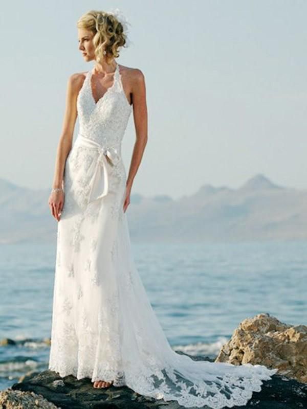 a woman in a white dress standing on rocks by the ocean with her back to the camera