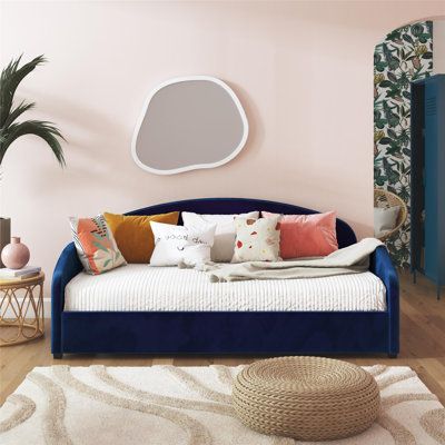 a living room with pink walls and blue couch, white rugs and potted plants