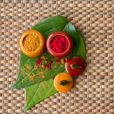 some spices are sitting on top of a green leaf and next to it is an orange, yellow, and red powder