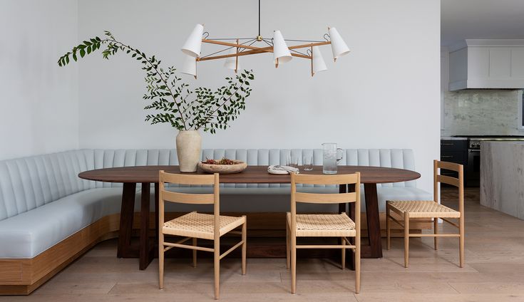 a dining room table with chairs and a bench in front of it, next to a potted plant