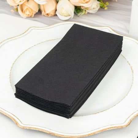 a stack of black napkins sitting on top of a white plate next to flowers