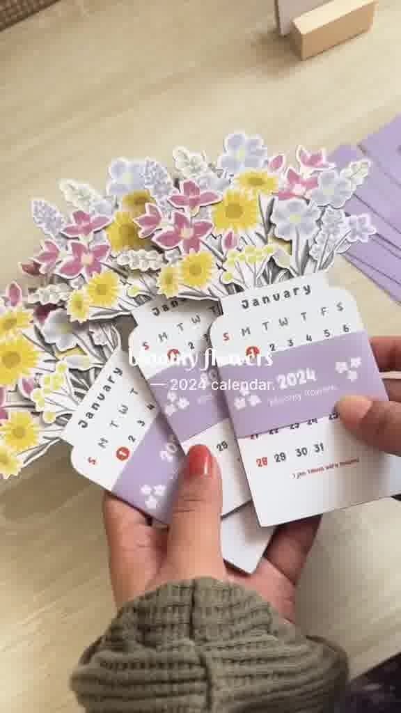 a person holding up some flowers on top of a wooden table next to a pile of cards