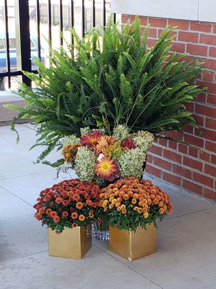 two gold vases with flowers in them sitting on the ground next to a brick wall