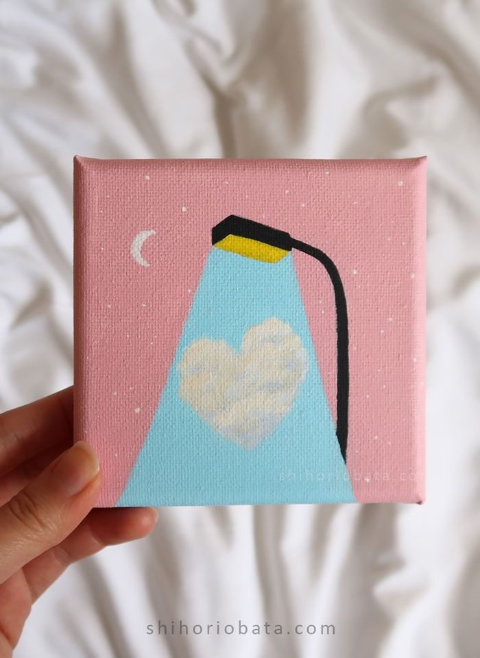 a hand holding up a small painting with a light on it's side and a heart in the middle