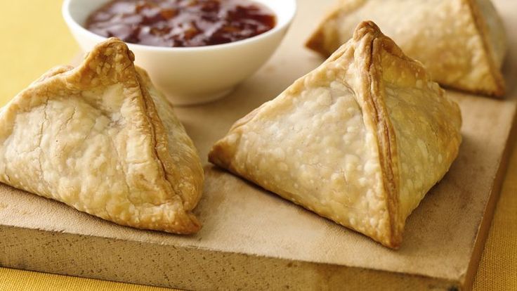 three pastries on a cutting board with dipping sauce