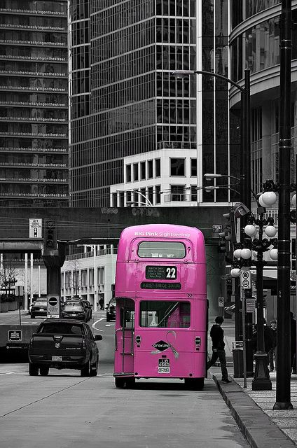 a pink double decker bus parked on the side of a road next to tall buildings