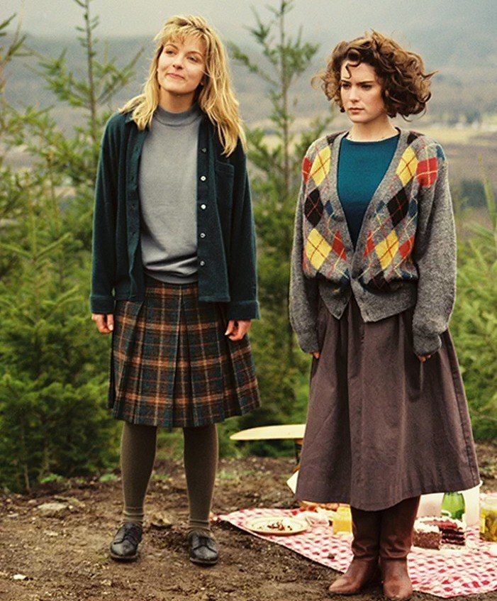 two young women standing next to each other on a blanket in front of some trees