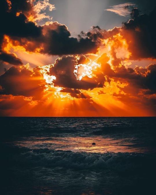 the sun is setting over the ocean with clouds in the sky and water below it