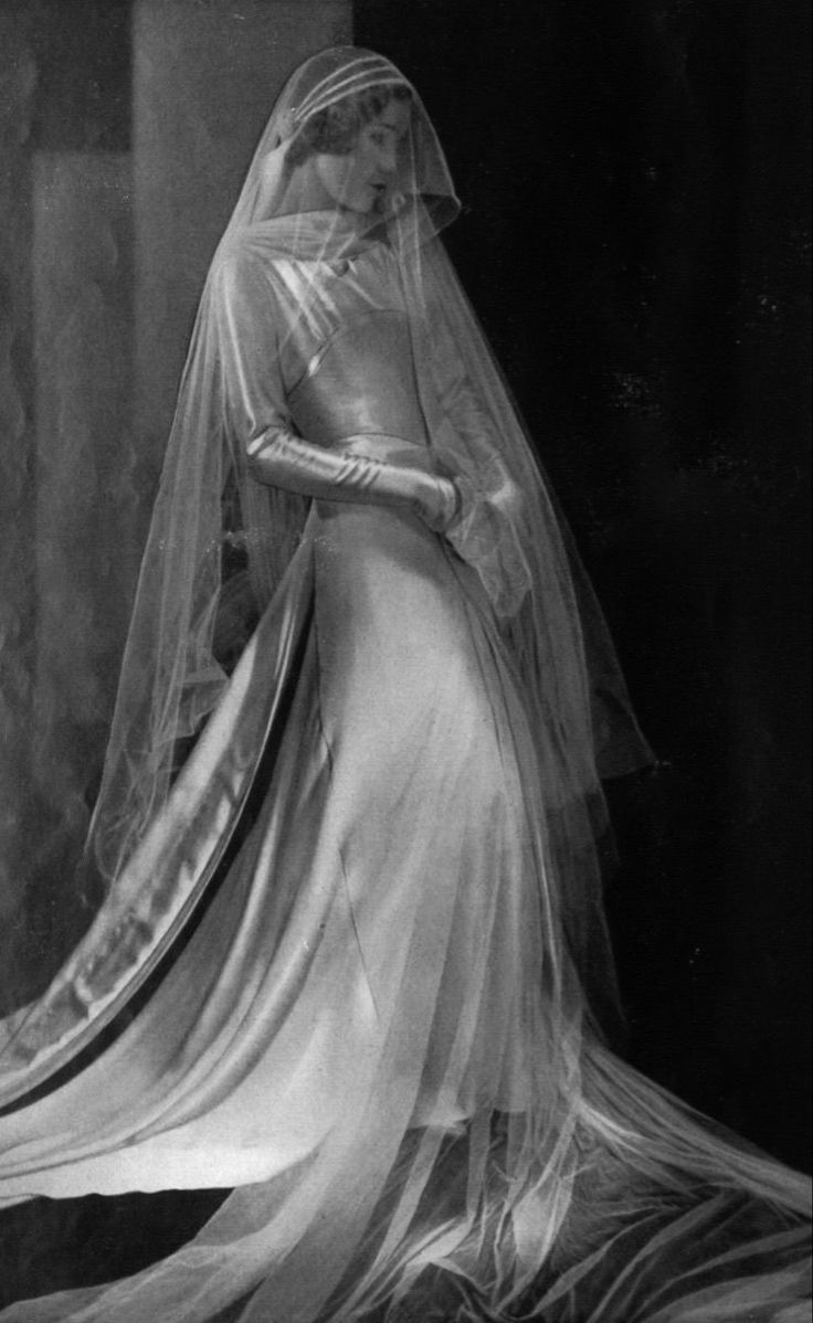 an old photo of a woman wearing a wedding dress and veil with her hand on her hip