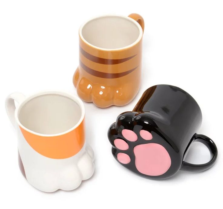 three coffee mugs with paw prints on them, one is orange and the other is black