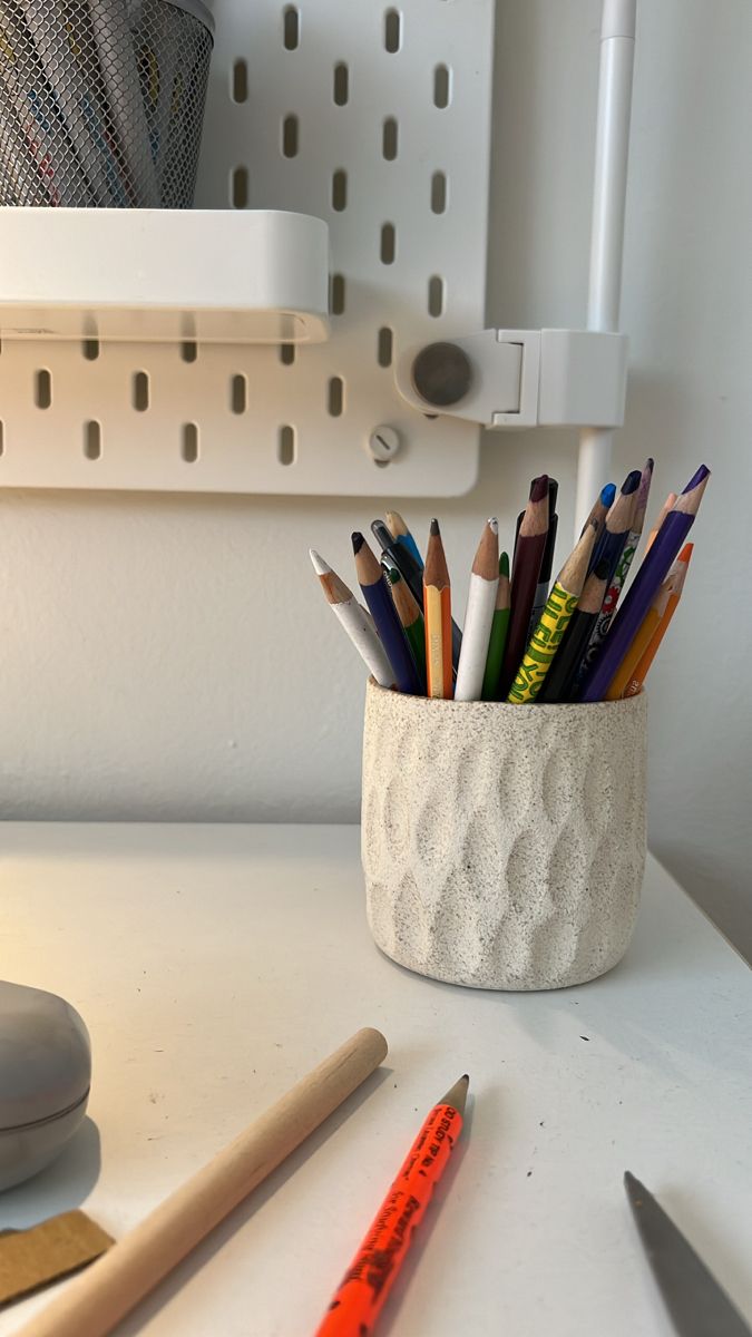 a cup full of pencils sitting on top of a white desk next to a mouse