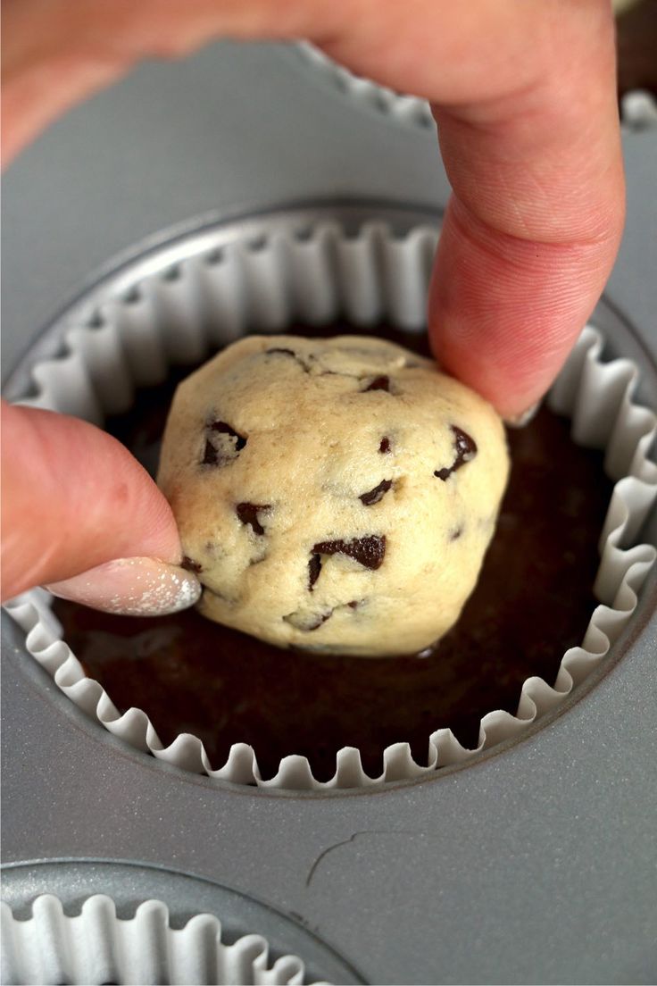 a hand picking up a chocolate chip cookie from a muffin tin