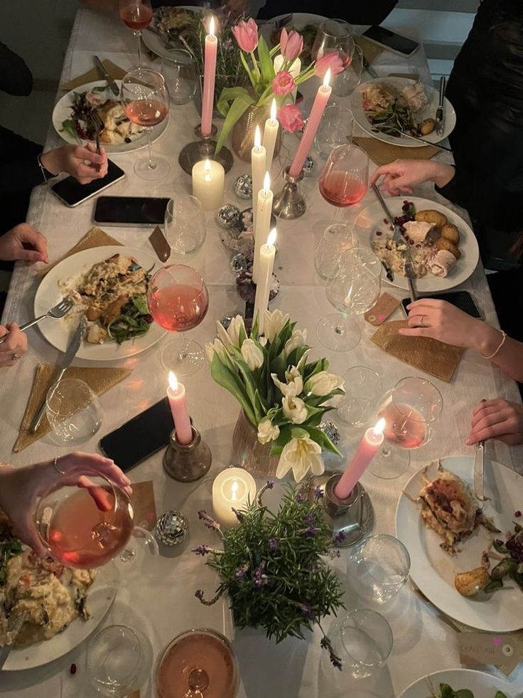 a group of people sitting around a dinner table with food and candles in the middle