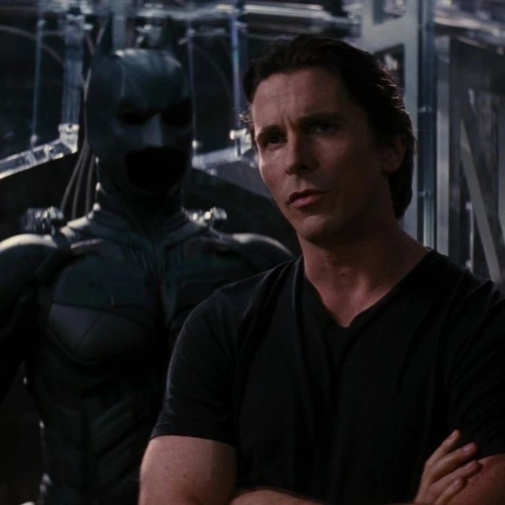 a man standing next to a batman character in the dark knight rises movie still has his arms crossed