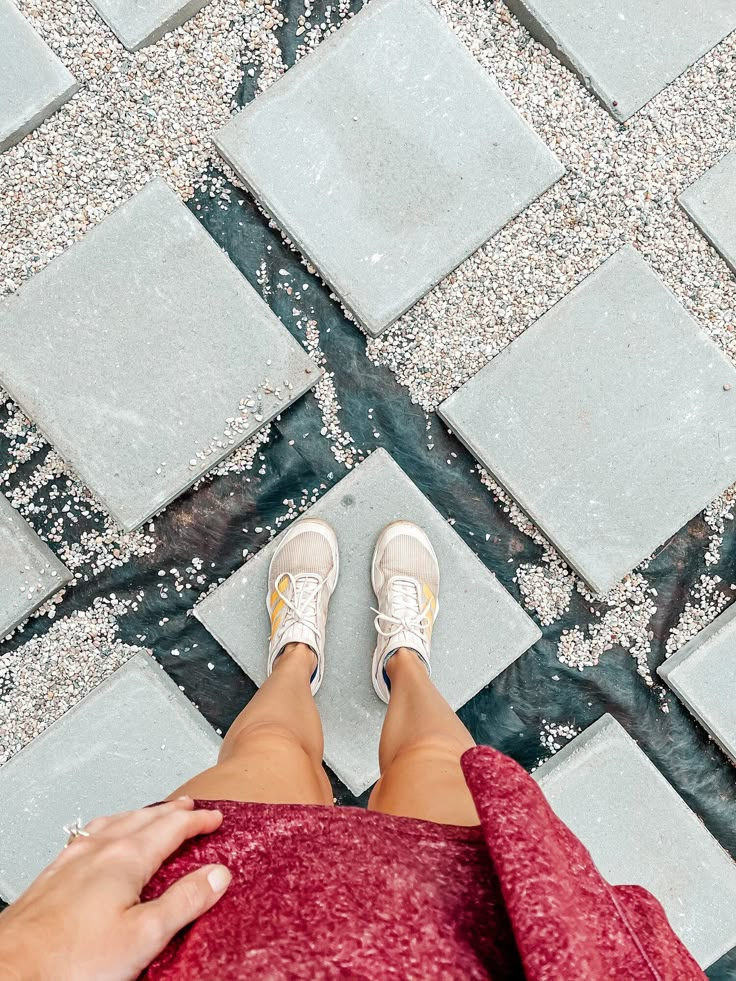 a woman's feet with white tennis shoes on standing in front of a tiled floor